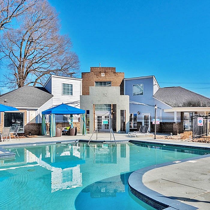 Inviting modern apartment complex with a sparkling outdoor pool and stylish cabanas under a clear blue sky.