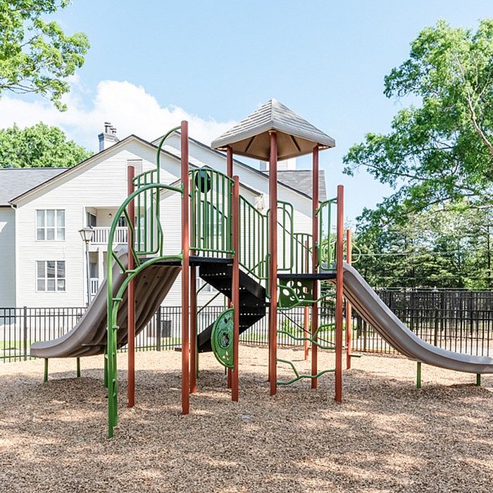 Charming apartment complex playground featuring vibrant slides and climbing structures surrounded by lush greenery, ideal for family living.