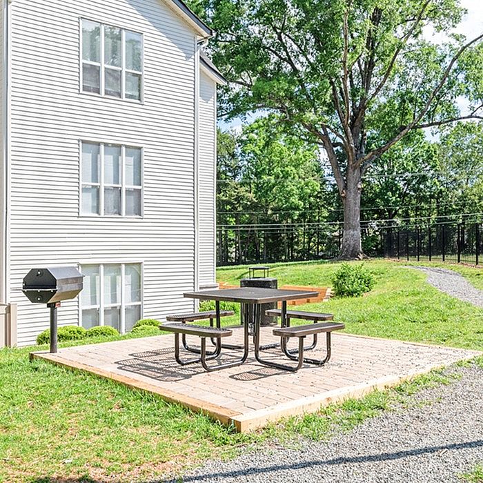 Charming outdoor space featuring a picnic area with a grill, nestled beside a modern apartment building surrounded by lush greenery.