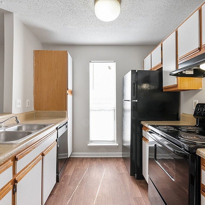Modern kitchen with sleek black appliances, natural wood cabinets, and ample sunlight.