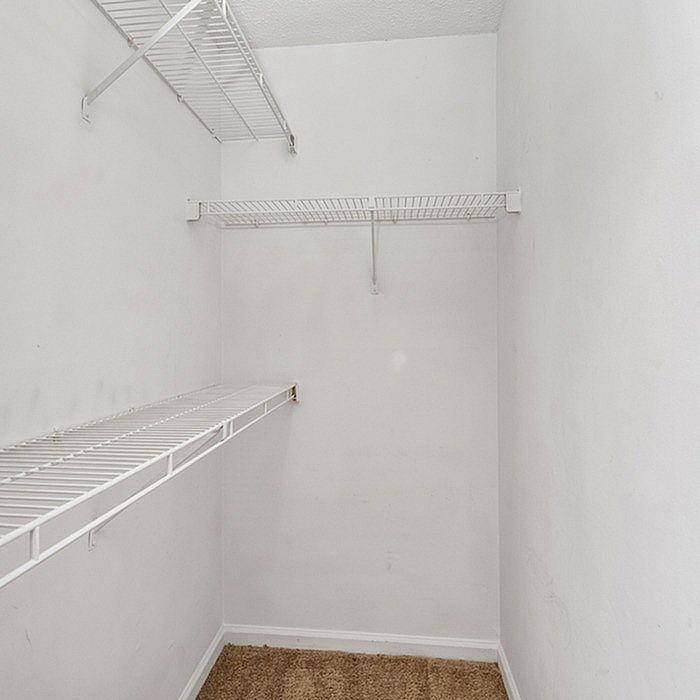 Spacious walk-in closet with sleek white wire shelving and plush carpet flooring, perfect for organized living.