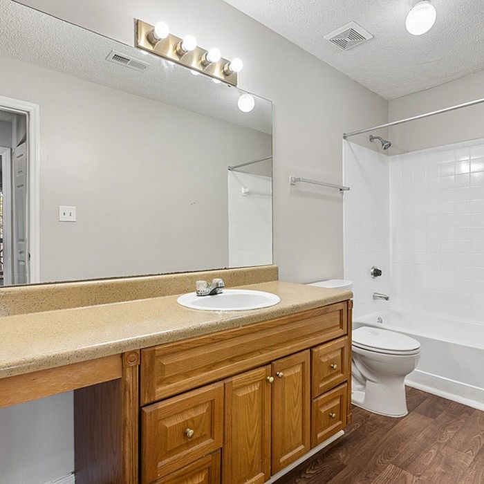 Bright and modern bathroom featuring sleek lighting, elegant wood cabinetry, and a pristine white bathtub.