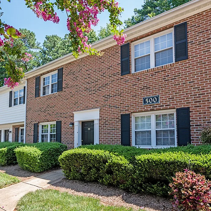 Charming brick townhouse with lush landscaping and blooming flowers, exuding a welcoming ambiance in a serene neighborhood.