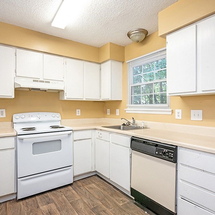 Bright kitchen with modern white cabinetry, efficient appliances, and warm wood flooring, ideal for culinary creativity.