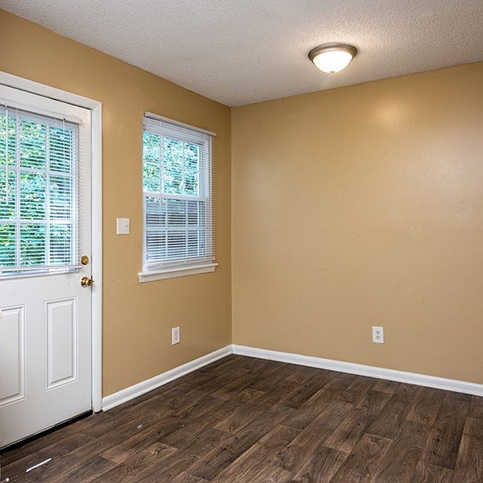 Inviting room with warm-toned walls, elegant wood flooring, and abundant natural light from a large window overlooking greenery.
