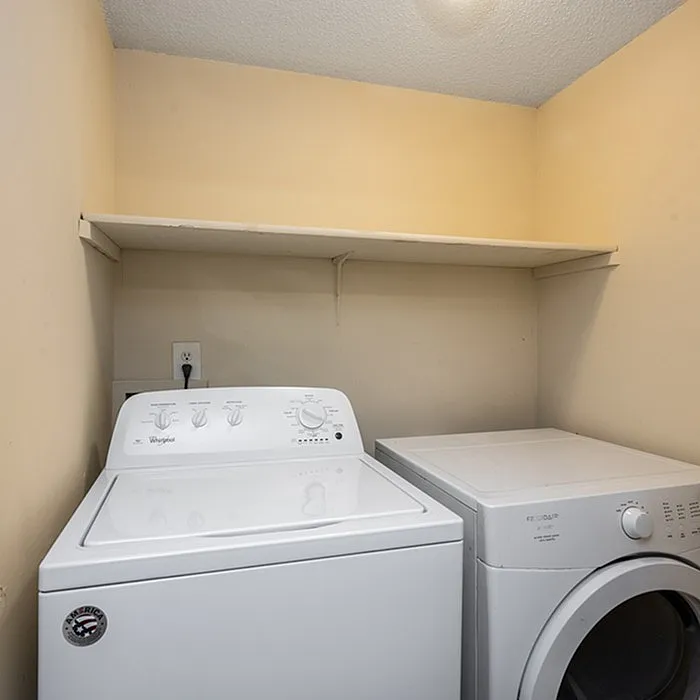 Cozy laundry area featuring a modern washer and dryer set beneath a practical storage shelf.