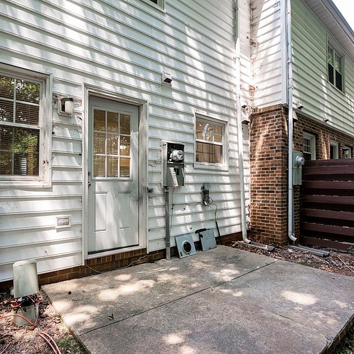 Charming side view of a modern white building exterior with a brick accent wall and a cozy private patio area.