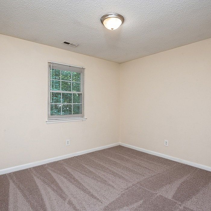 Bright, freshly carpeted room with a large window allowing abundant natural light, perfect for a cozy bedroom or home office.