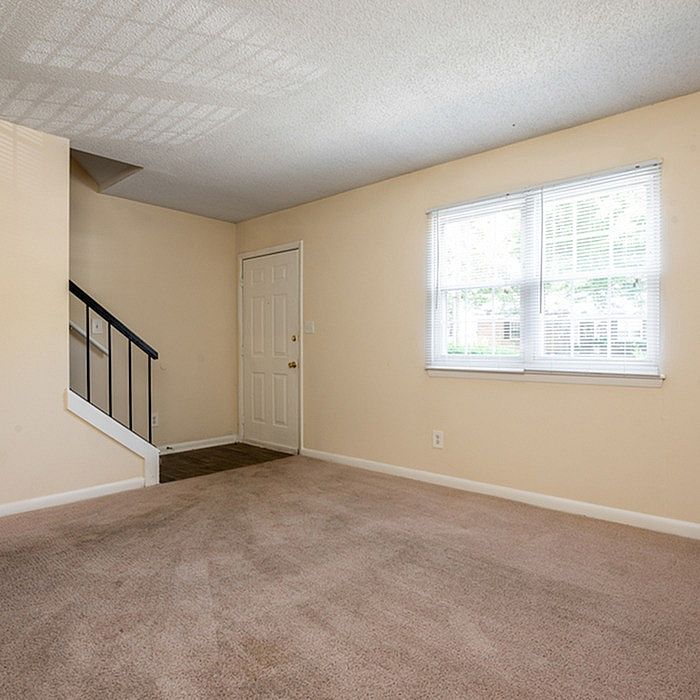 Bright, inviting living room with plush carpeting, large window for natural light, and elegant staircase.