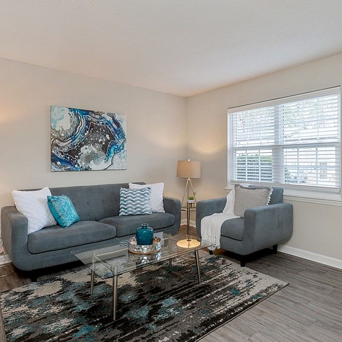 Bright and inviting living room with modern gray sofas, abstract wall art, and a stylish glass coffee table, perfect for relaxation.