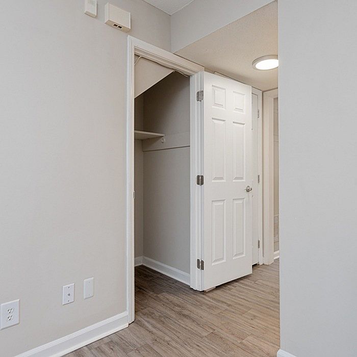 Inviting apartment hallway with a modern open closet, neutral walls, and sleek wood flooring.