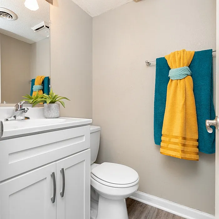 Charming bathroom with modern white vanity, sleek fixtures, and vibrant yellow and teal towel accents complementing the fresh decor.