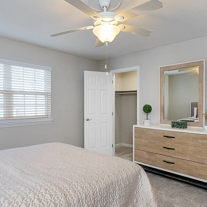 Bright and inviting bedroom with a cozy bed, stylish dresser, elegant ceiling fan, and spacious walk-in closet.