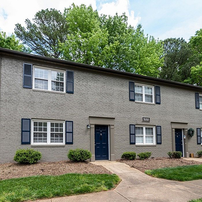 Charming two-story apartment building with classic brick exterior, surrounded by lush greenery and vibrant blue shutters.