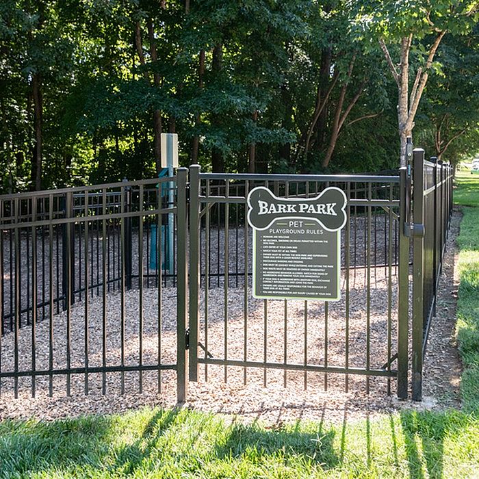 Inviting fenced Bark Park with plush grassy surroundings and shaded areas, perfect for pet playtime and relaxation.