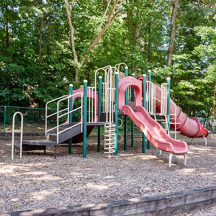Charming playground featuring vibrant slides and tunnels surrounded by lush greenery. Ideal for family-friendly apartment living.