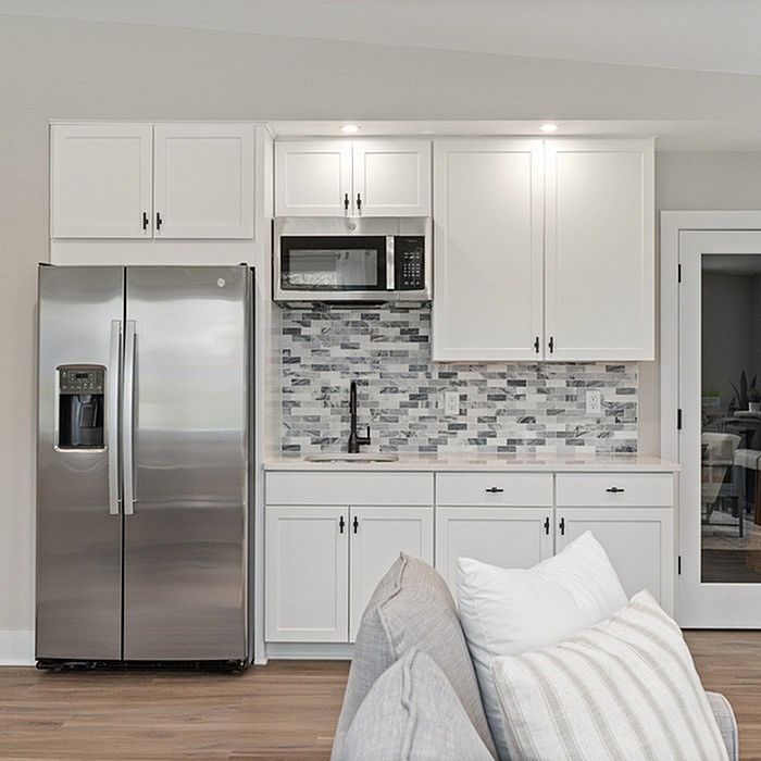 Modern kitchen with sleek stainless steel refrigerator, elegant white cabinets, and stylish mosaic backsplash.