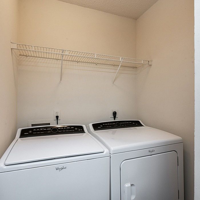 Modern laundry room with sleek washer and dryer set against a neutral backdrop, featuring a convenient overhead shelf.