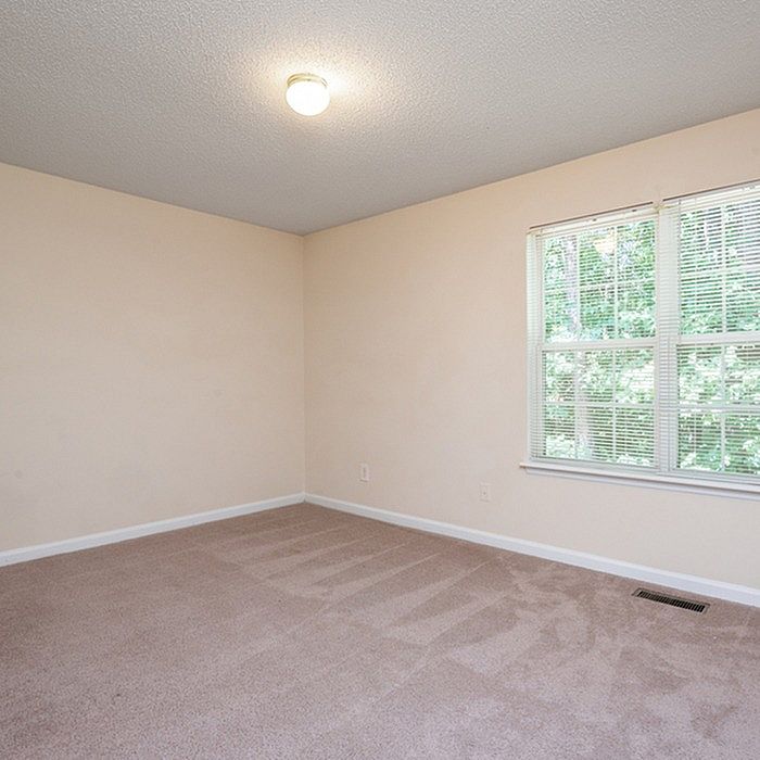 Bright and airy empty bedroom with plush carpet and large window offering serene outdoor views.