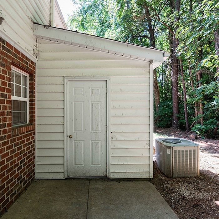Charming house entrance with white siding and a serene wooded backdrop, offering a tranquil retreat.