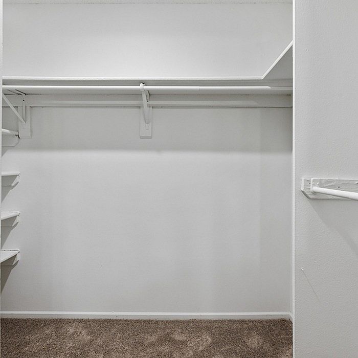 Spacious walk-in closet with white walls and carpeted flooring, perfect for ample storage and organization.
