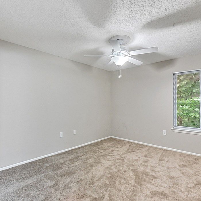 Bright and spacious room with plush carpet, neutral walls, and a ceiling fan, ideal for a serene living space.