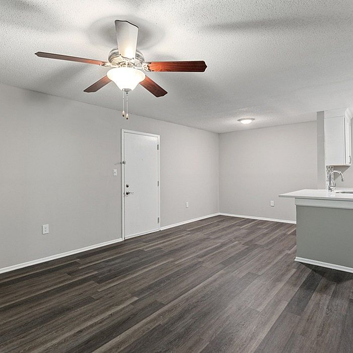 Modern apartment with elegant ceiling fan and sleek wooden flooring, featuring an inviting open-plan layout with a bright kitchen area.