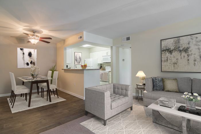 Modern open-concept living and dining area with elegant furnishings, cozy gray sofa, sleek armchair, and stylish decor. Bright kitchen with white cabinetry completes the inviting space.