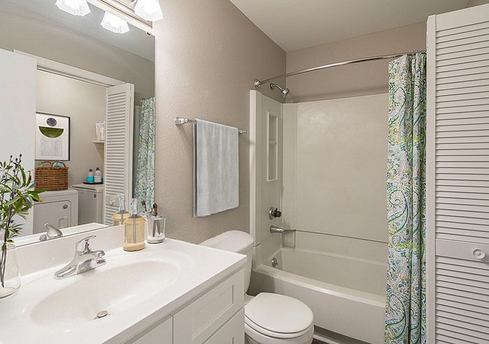 Bright and modern bathroom featuring sleek white fixtures, a decorative shower curtain, and a glimpse of a cozy laundry area in the background.