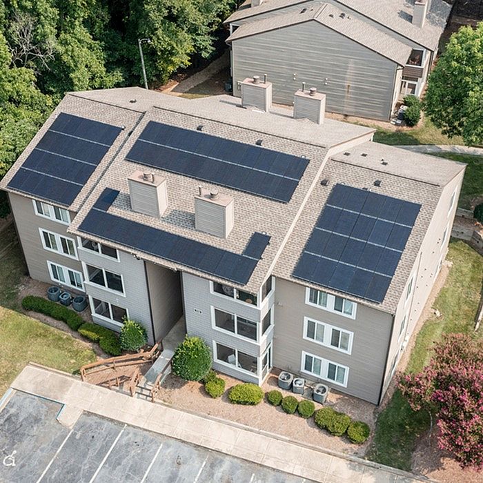 Aerial view of a modern apartment building with solar panels on the roof, surrounded by lush greenery and a well-maintained landscape.