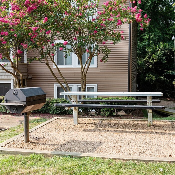 Charming apartment exterior view with a blooming garden, picnic bench, and barbecue grill area, perfect for outdoor gatherings.