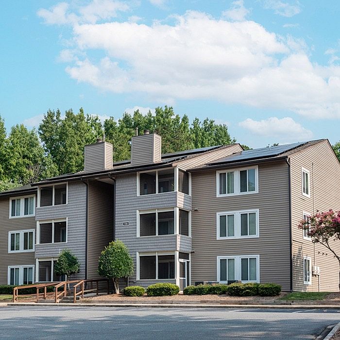 Charming apartment complex with modern design, ample windows, and surrounded by lush greenery under a clear blue sky.