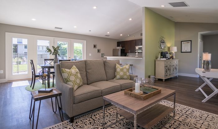Chic open-concept living area with modern decor, featuring a cozy gray sofa, stylish wooden coffee table, and a dining nook with outdoor views through French doors.