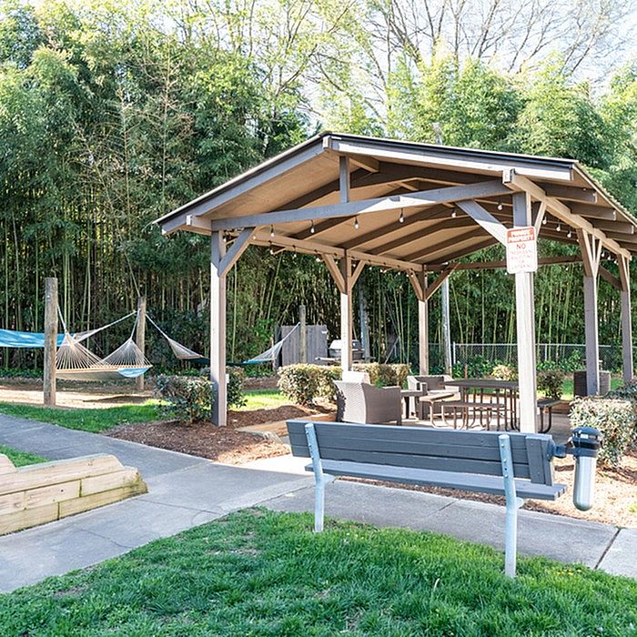 Charming outdoor pavilion with cozy seating and hammocks, surrounded by lush greenery, offering a relaxing community space.