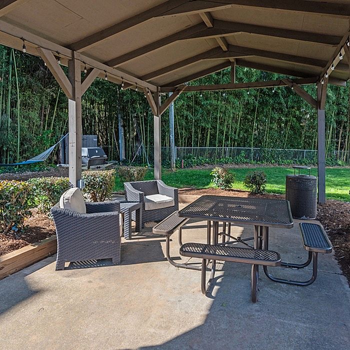 Charming outdoor patio under a wooden pergola with cozy seating and picnic table, surrounded by lush greenery for a peaceful retreat.