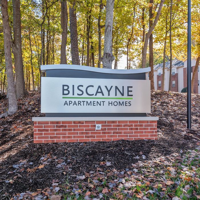Inviting sign for Biscayne Apartment Homes set amid a serene wooded landscape, offering tranquil living in a picturesque setting.