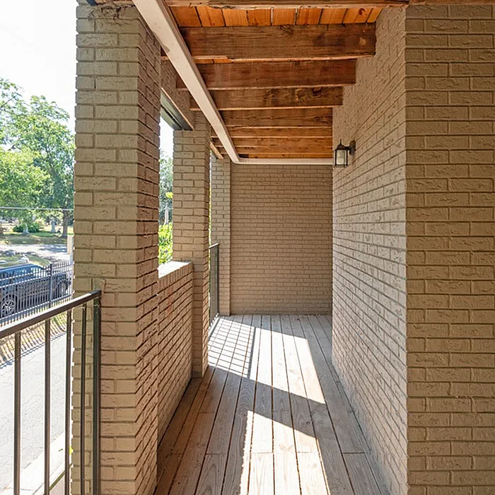 Inviting and sunlit brick balcony with wooden beams overlooking serene greenery.