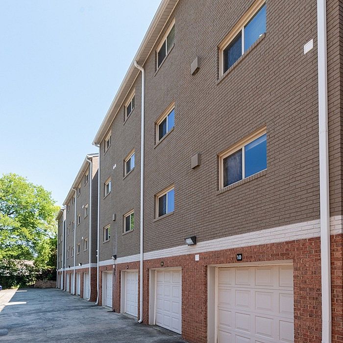 Charming brick apartment building with multiple garages, featuring modern windows and surrounded by lush greenery.