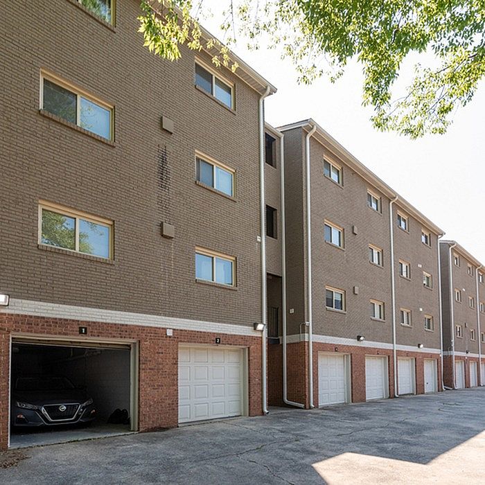 Modern apartment building with multiple levels, featuring spacious garages and surrounded by lush greenery.