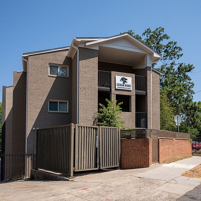 Modern Cedar Oaks condominium building with stylish brick exterior and spacious balconies, nestled amidst vibrant greenery.