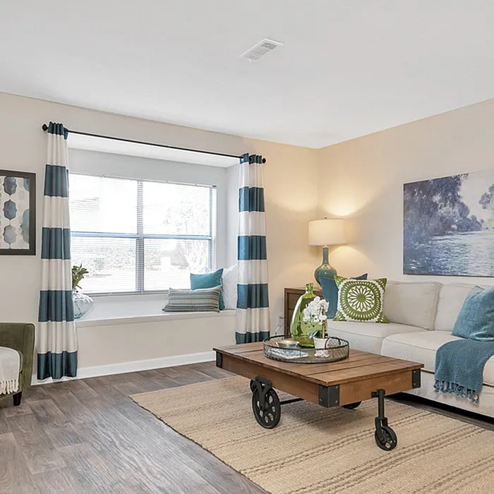 Bright, cozy living room with stylish decor, featuring a large window nook, striped curtains, and a chic coffee table on elegant wooden flooring.