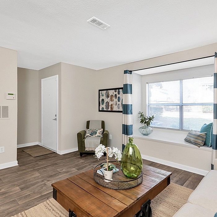 Inviting living room with elegant decor, featuring a cozy armchair, stylish coffee table with chic centerpiece, and a bright window nook adorned with plush cushions.