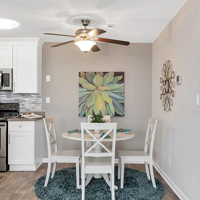 Charming dining area featuring a modern round table set with white chairs, elegant wall art, and a chic kitchen backdrop.