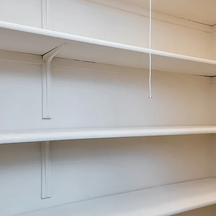 Spacious built-in shelving unit in a bright room with a pull string light, perfect for stylish storage solutions.