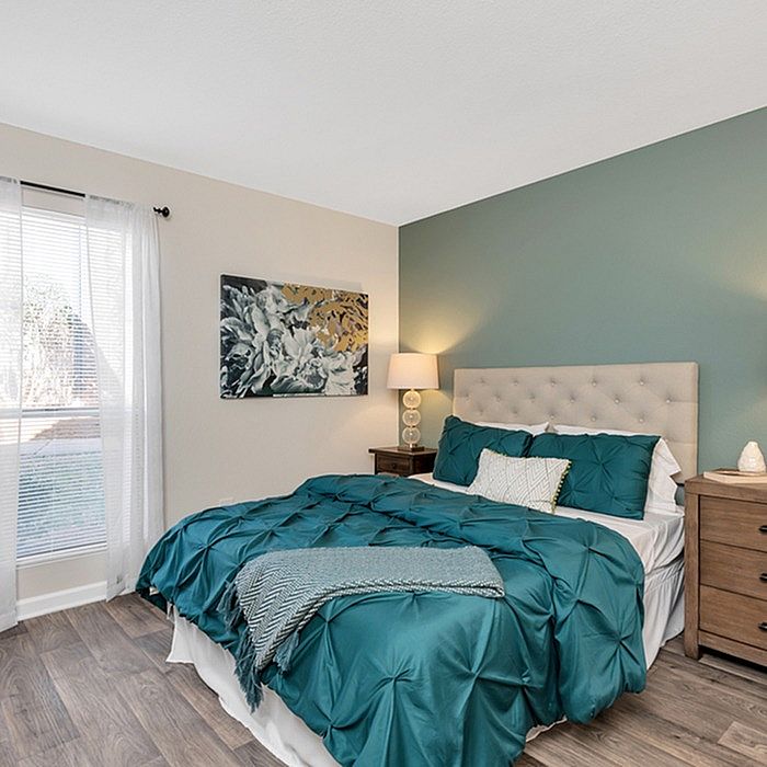 Charming bedroom with stylish teal bedding, elegant artwork, and natural light from large windows.