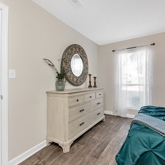 Elegant bedroom with a chic dresser, round decorative mirror, and sunlit window, showcasing modern charm and comfort.