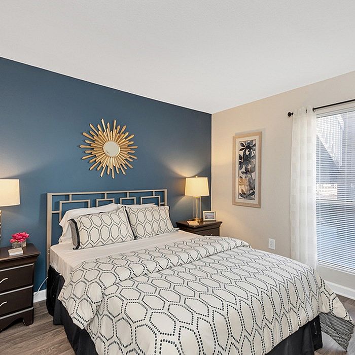 Elegant bedroom with stylish sunburst mirror, cozy bedding, and ambient lighting.