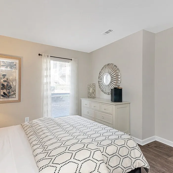 Inviting bedroom with stylish decor, featuring a plush bed, elegant dresser, and bright natural lighting through a large window.