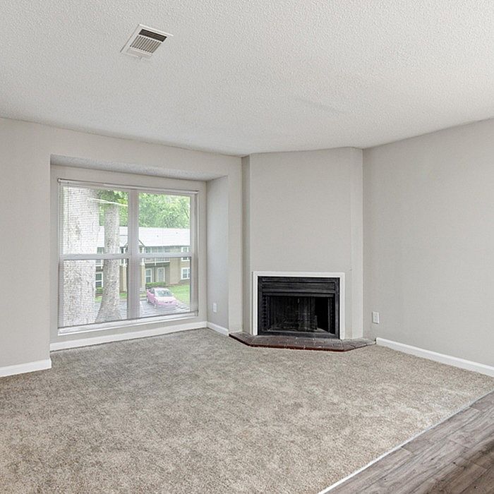 Bright and airy living room with a large window, cozy fireplace, and plush carpet flooring.