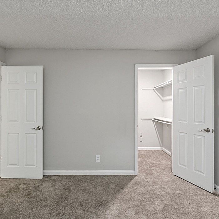 Inviting bedroom featuring plush carpeting and a spacious walk-in closet with modern shelving, enhancing comfort and style.
